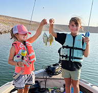 Dos niñas, cada una sosteniendo un pez pequeño capturado en un barco de pesca