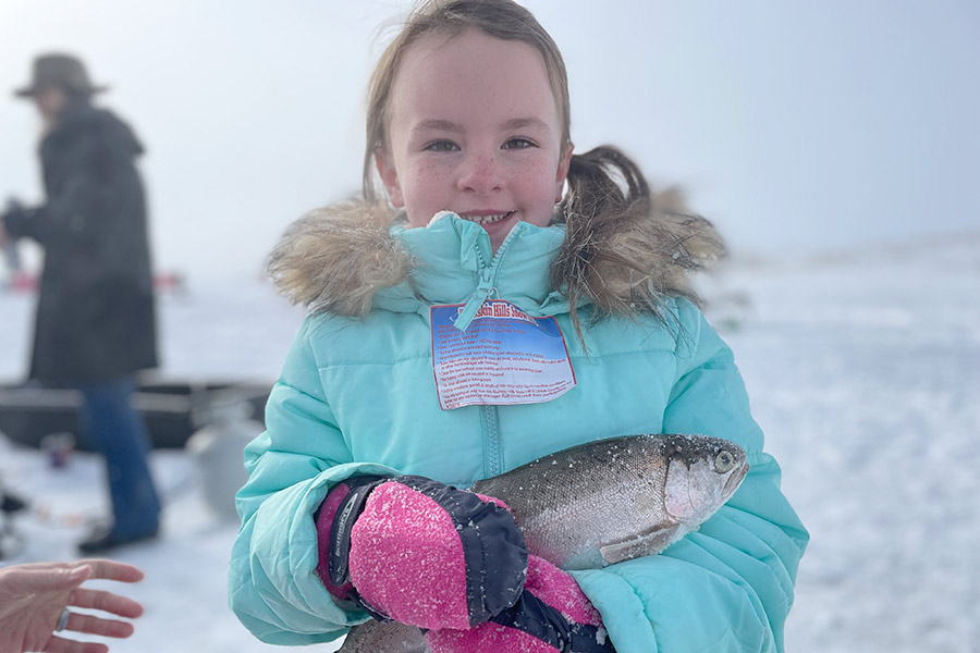 Girl standing on a frozen-over lake, holding a caught fish